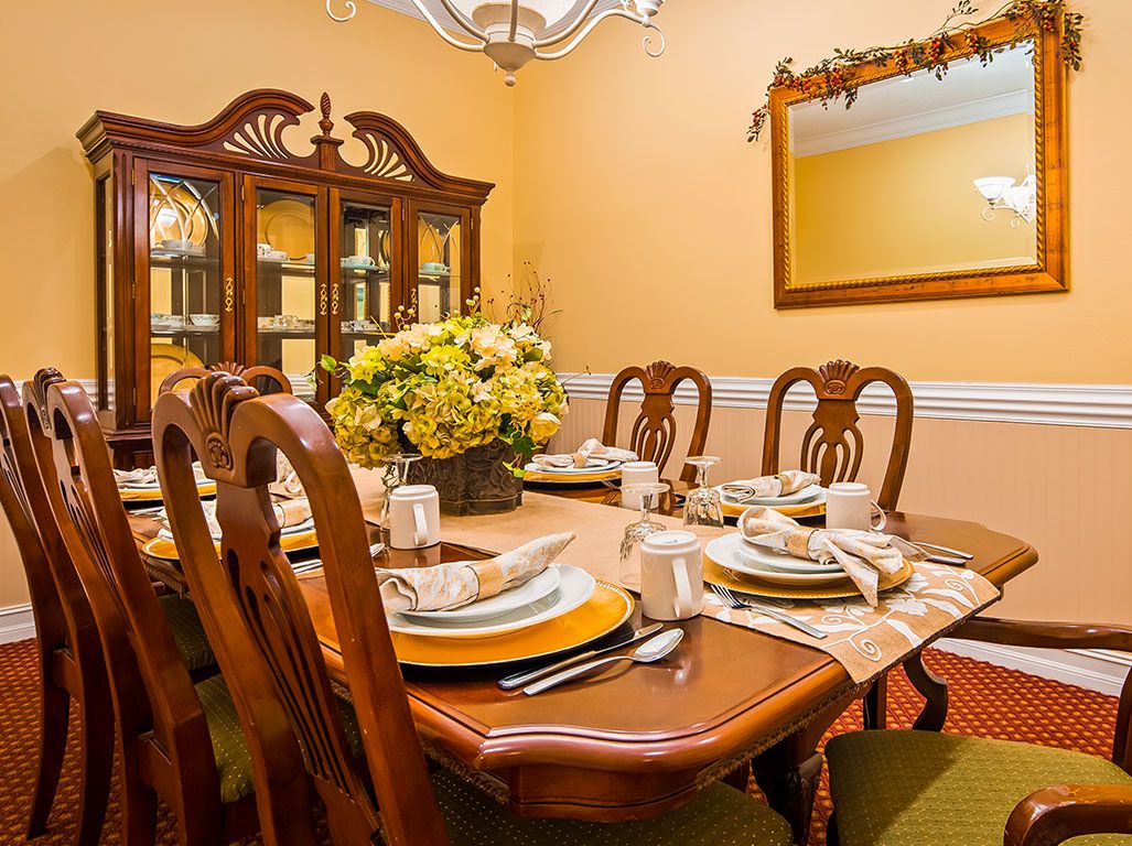 A warmly lit dining room with a wooden table set for a meal, adorned with elegant tableware and a flower arrangement.