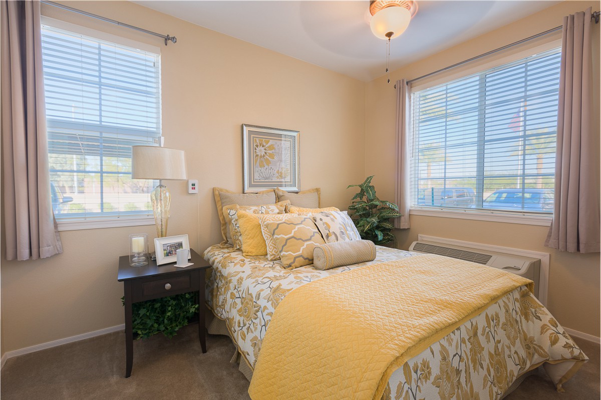 A cozy and well-lit bedroom with elegant decor featuring a neatly made bed, bedside table, and soft yellow accents.