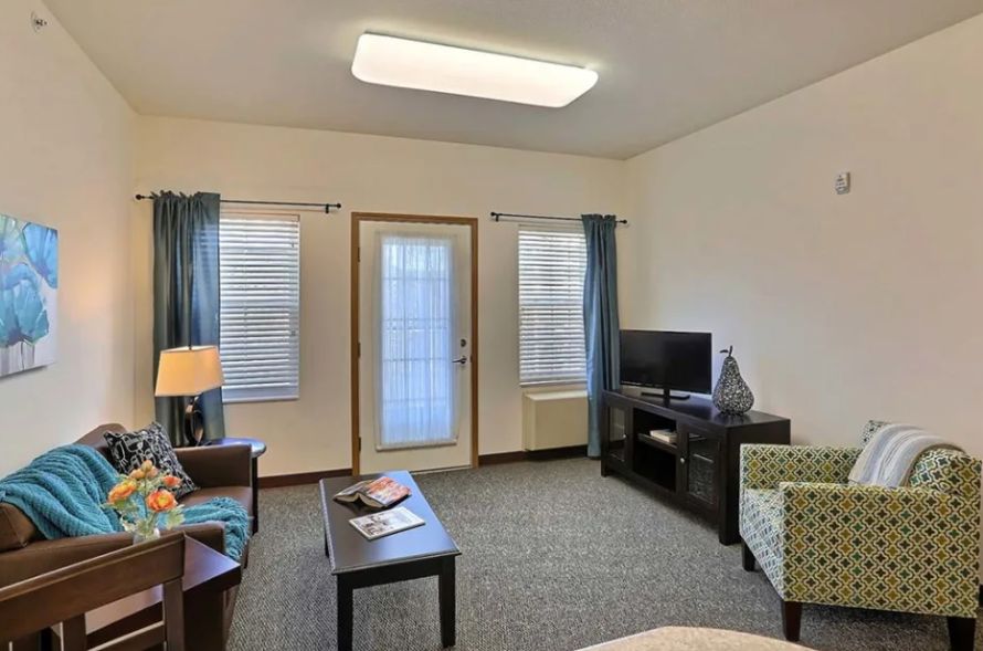 A cozy living room with a sofa, television, and coffee table, featuring windows with blue curtains.