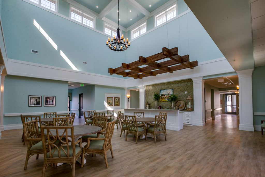 A spacious dining area with high ceilings, featuring a chandelier and wooden furniture, illuminated by natural light.