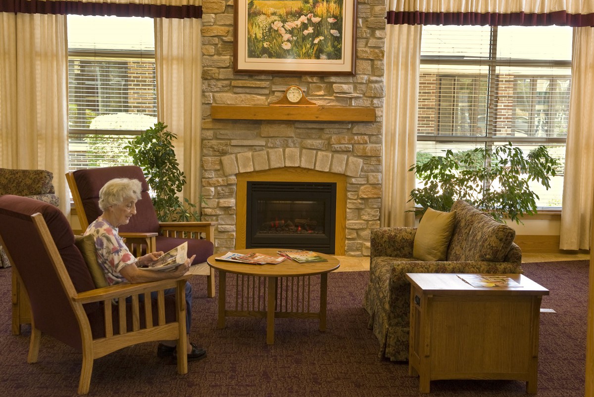 An elderly person sitting and reading in a cozy living room with a fireplace.