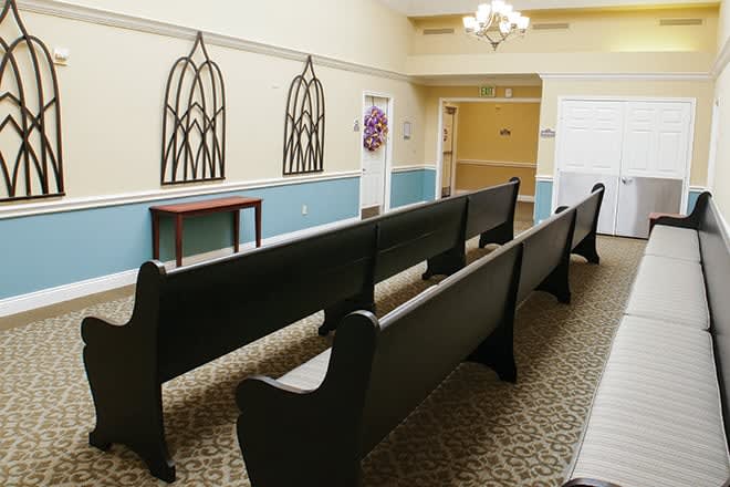 A small chapel with rows of dark wooden pews and decorative wall elements.