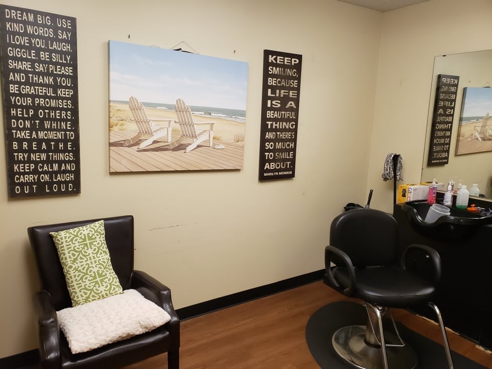 A cozy hair salon interior with a comfortable styling chair, wall art, and decorative cushions.