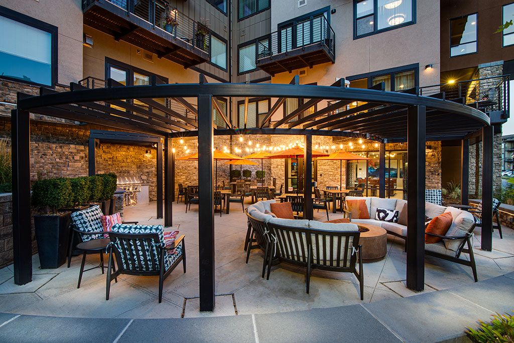 A cozy outdoor patio with seating and string lights, surrounded by apartment buildings at dusk.