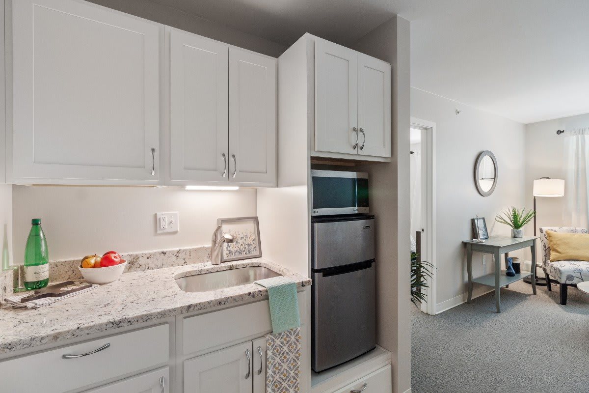 A modern kitchen with white cabinets, countertop, sink, and a compact refrigerator.