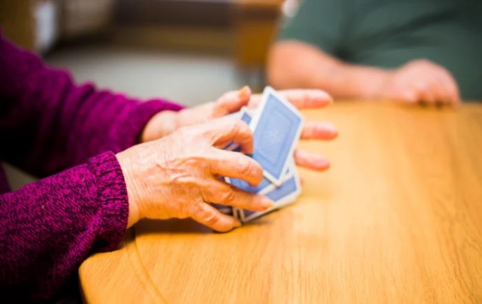 A person shuffling playing cards on a wooden table.