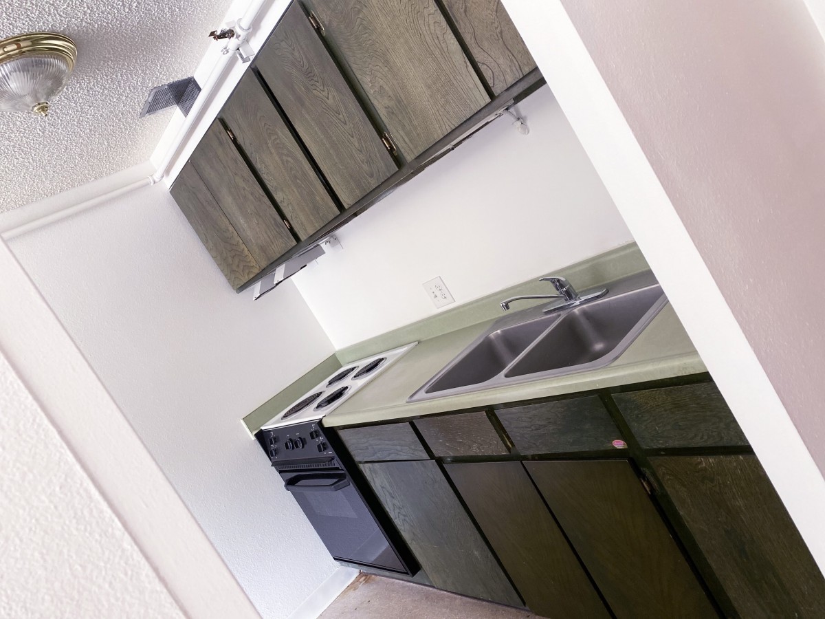 A compact kitchen with wooden cabinets, a double sink, and an electric stove.