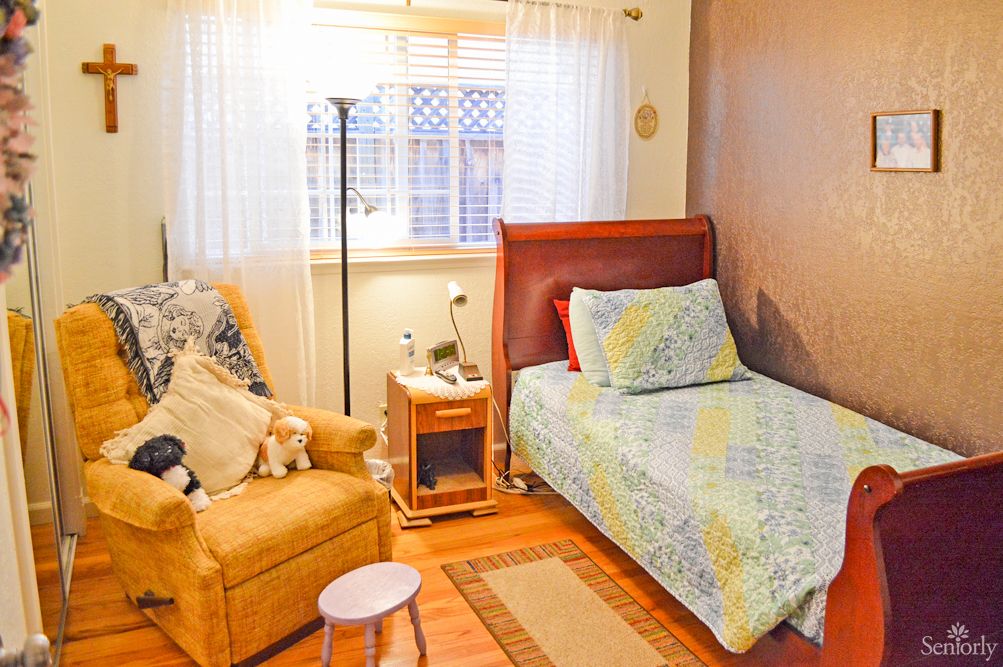 A cozy bedroom with a single bed, armchair, and a small side table by the window.