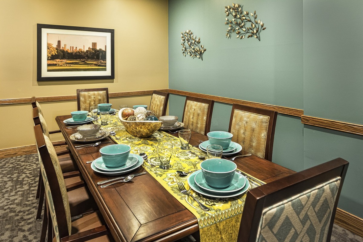 A dining room with an elegant table setting featuring blue dishes and a yellow table runner, complemented by wall art and a photograph.