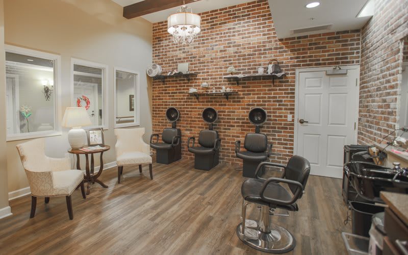 A modern salon interior featuring a brick accent wall, hair drying stations, and stylish seating.