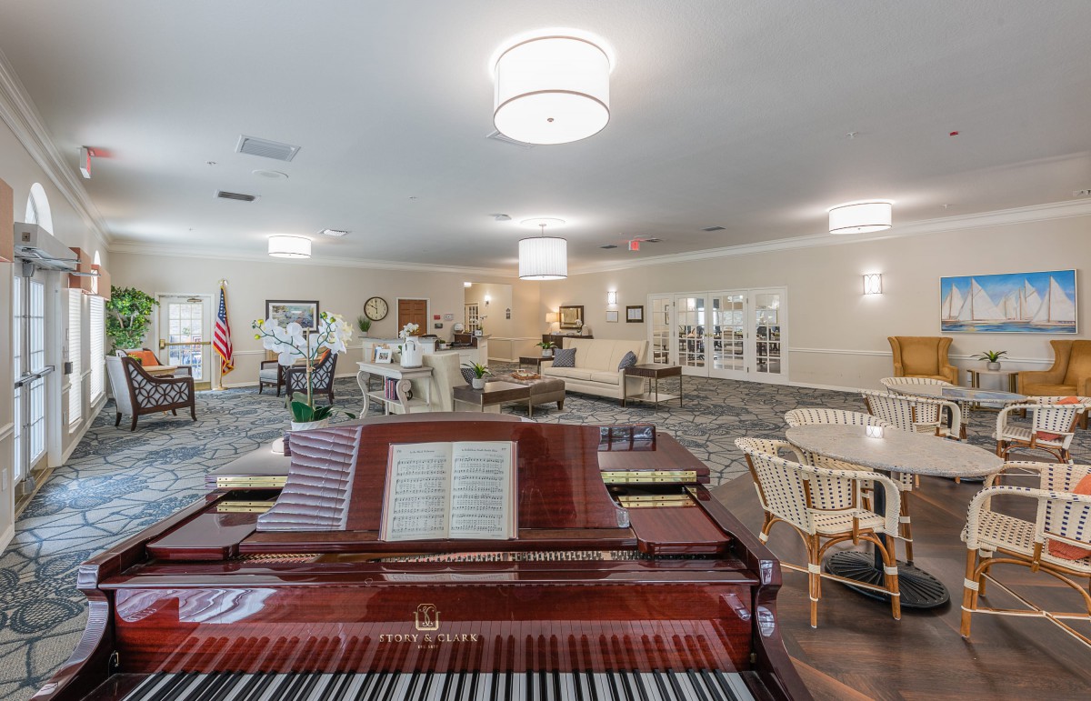 A spacious lounge area featuring a grand piano and ample seating, illuminated by stylish chandeliers.