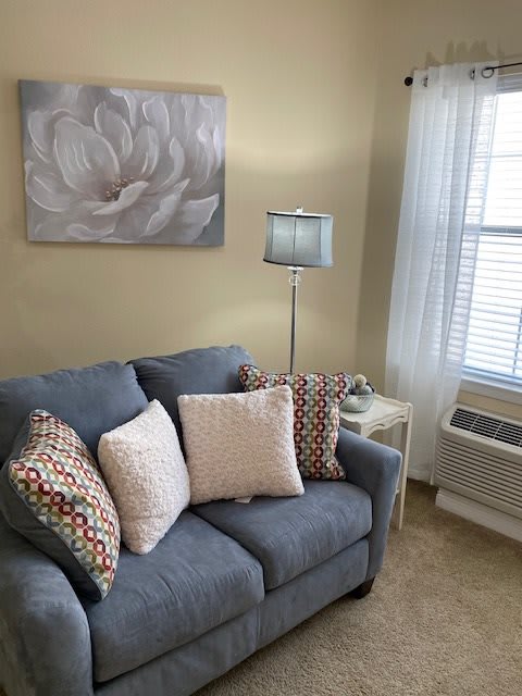 A cozy living room with a blue sofa, decorative cushions, a floor lamp, and a floral painting.