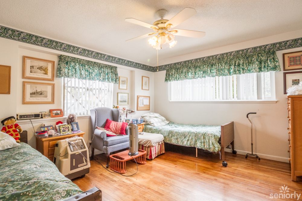 A cozy bedroom with twin beds, decorated with floral curtains and various frames on the walls.