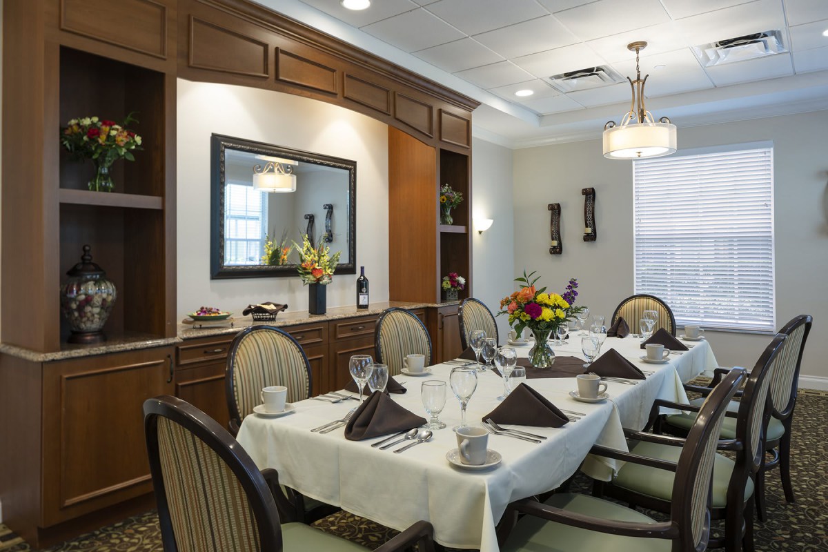 An elegantly set dining room with a neatly arranged table, featuring flowers and fine dining settings.