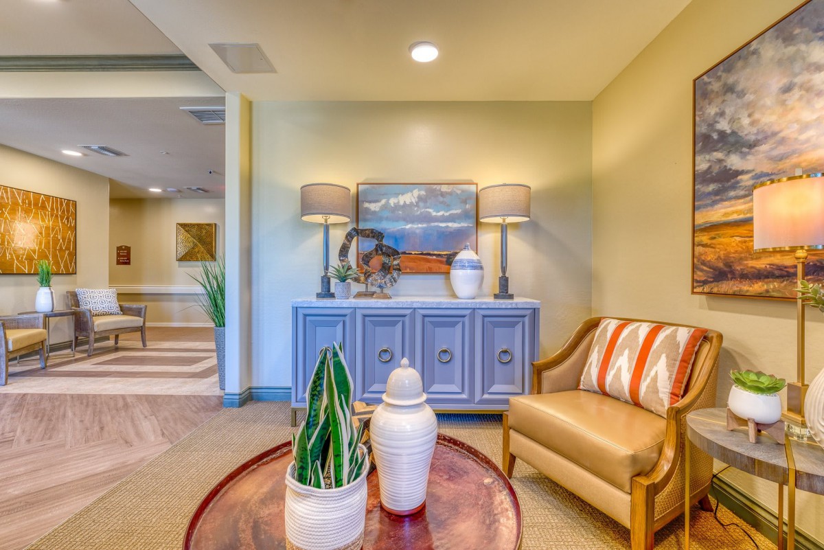 A cozy living room setting featuring a chair, decorative cabinet with lamps, and artwork on the wall.