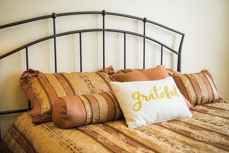 A neatly arranged bed with decorative pillows, featuring one with the word 'Gratitude'.