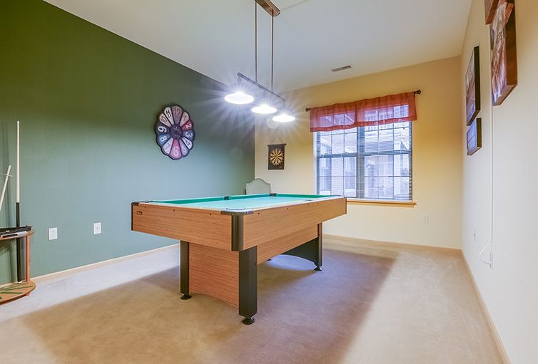 A cozy game room featuring a billiards table, a large wall clock, ambient lighting, and a window with natural light.