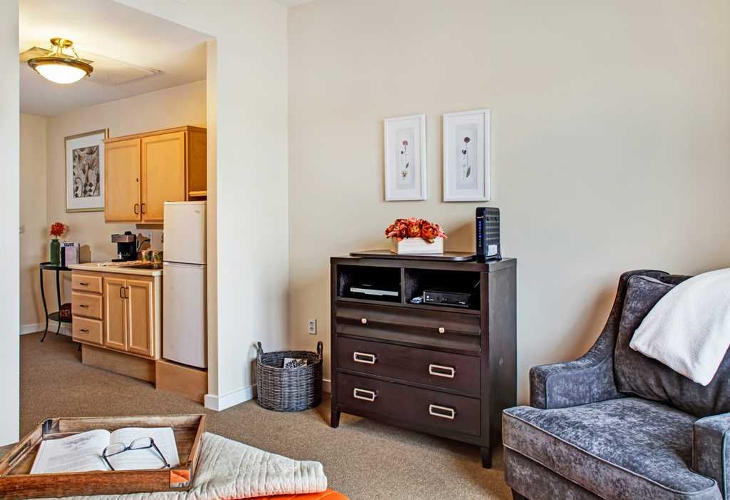 A cozy living room area with a view into the kitchen, featuring a cabinet, chair, and decorative accents.