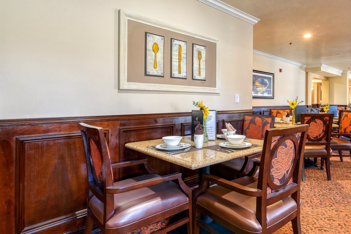 A cozy dining area in a restaurant with a table set for two, featuring elegant wooden chairs and framed wall art.