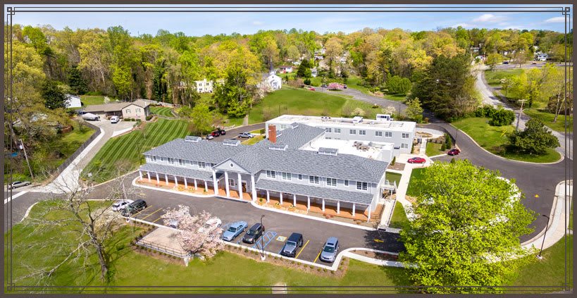 Aerial view of a suburban building with a parking lot surrounded by trees and roads.