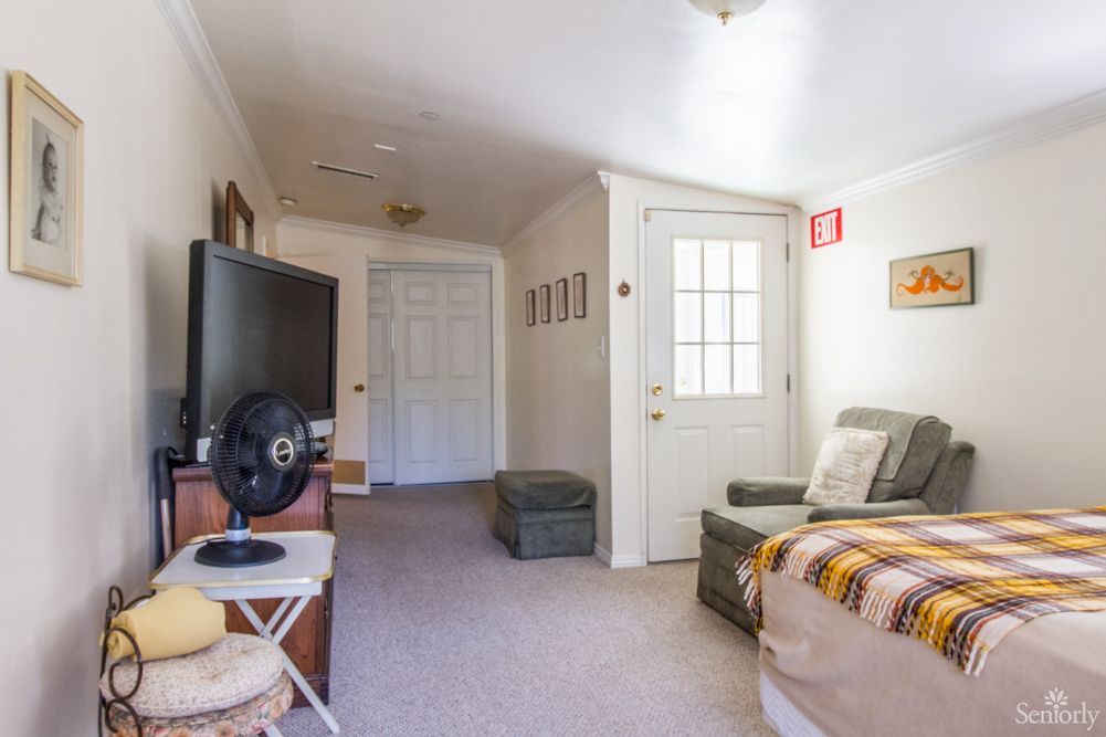 A cozy living room with a TV, couch, and fan, featuring a door leading to another area.