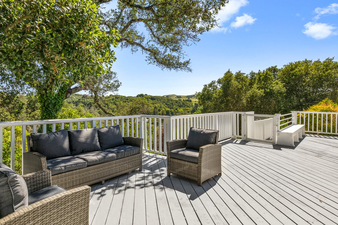 A scenic outdoor deck with comfortable seating, surrounded by lush greenery and trees.