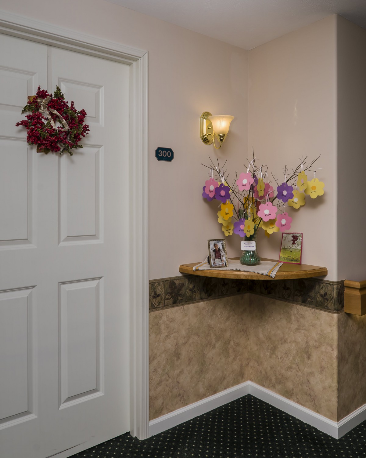 A hallway with a decorated door, floral arrangement, and wall sconce lighting.