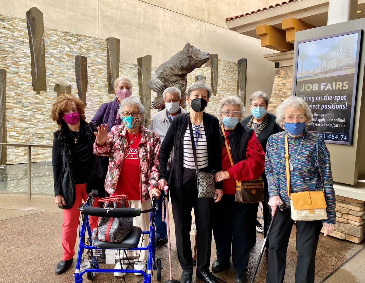 A group of seniors wearing masks, gathered indoors, with one using a walker.