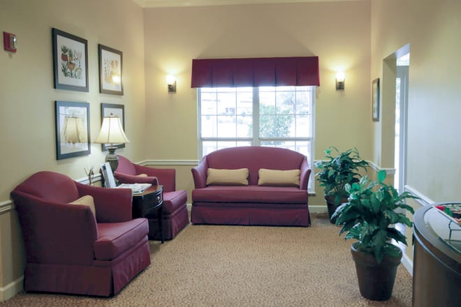 A cozy living room with a sofa and matching armchairs, decorated with indoor plants and framed wall art.