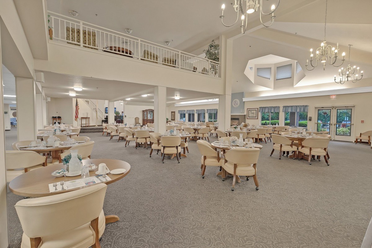 A spacious dining room with neatly arranged tables and chairs under bright lighting and a prominent chandelier.