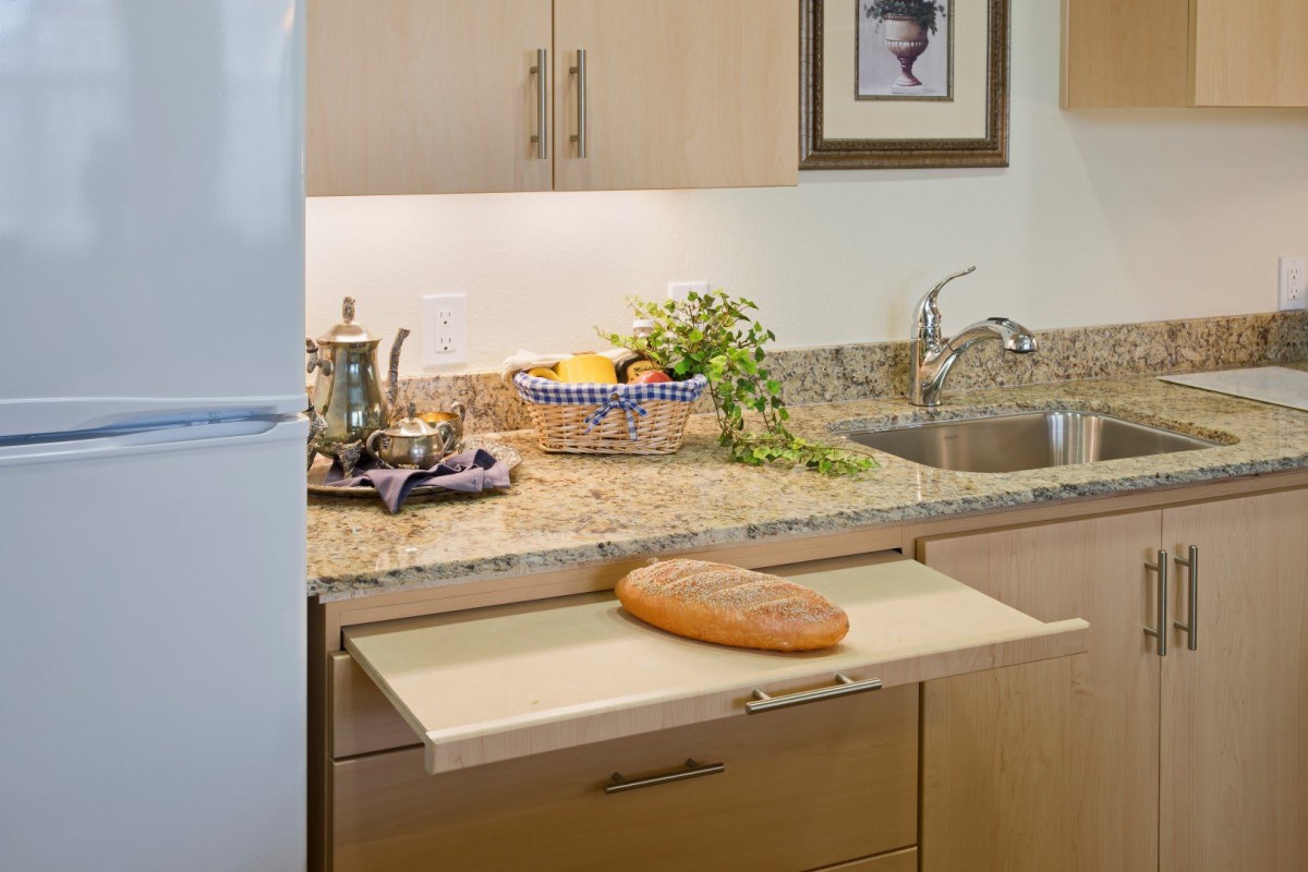 A cozy kitchen setup featuring a pull-out cutting board with a loaf of bread, surrounded by kitchen decor and a granite countertop.