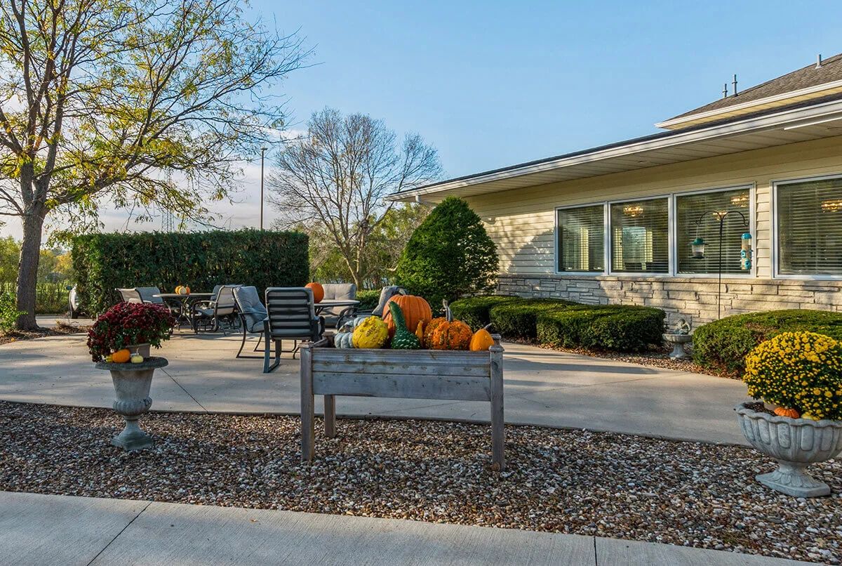A cozy outdoor patio decorated with pumpkins for autumn, featuring a bench and garden area.