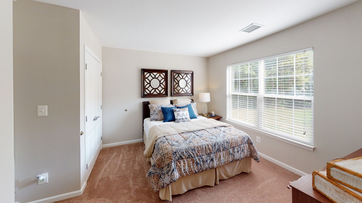 A cozy bedroom interior with a neatly made bed, decorative wall art, and natural light streaming through the window.