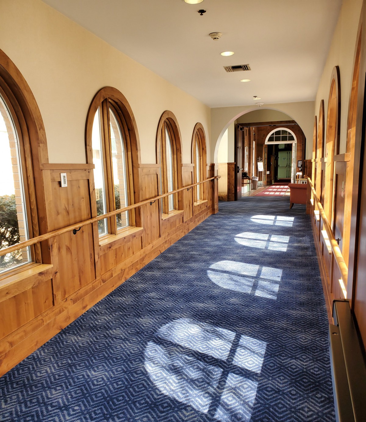 A sunlit hallway with arched windows and a blue carpet.