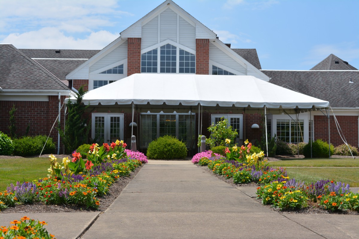 A beautiful garden pathway leading to a large building with a white awning.