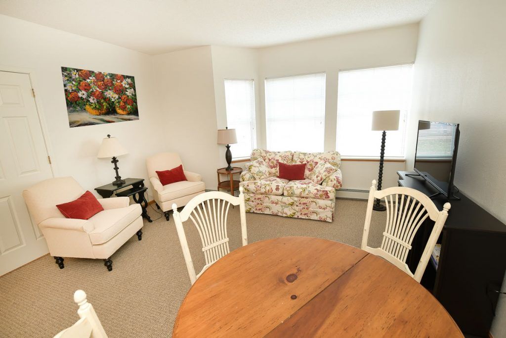 A cozy living room with floral and neutral tones, featuring a sofa, armchairs, and round wooden table.