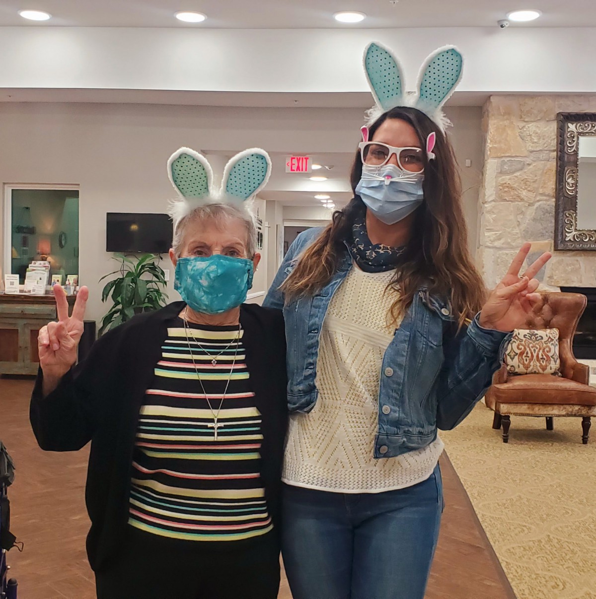 Two people wearing bunny ears and masks, posing with peace signs indoors.