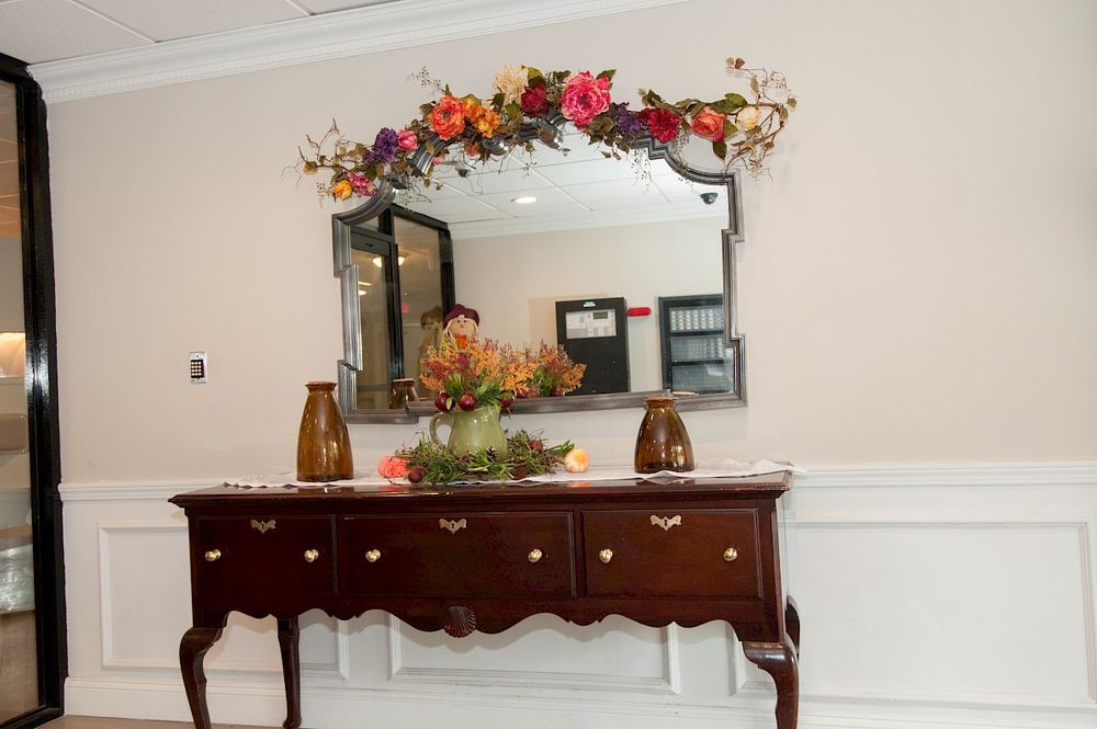 A beautifully decorated sideboard with a mirror adorned with colorful flowers and vases, creating an elegant interior display.
