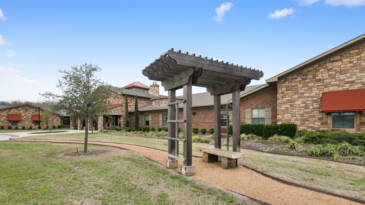 An outdoor view of a building with a pergola and landscaped pathway.