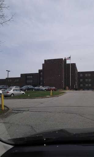 A view of a brick hospital building with an adjacent parking lot and flags flying.