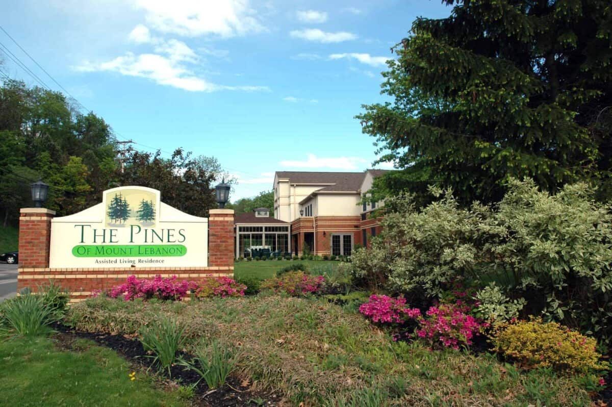 A landscaped area with a sign and building, surrounded by flowers and trees under a clear sky.