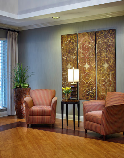 A cozy living room setup featuring two brown chairs, decorative artwork on the wall, a lamp, and a touch of greenery.