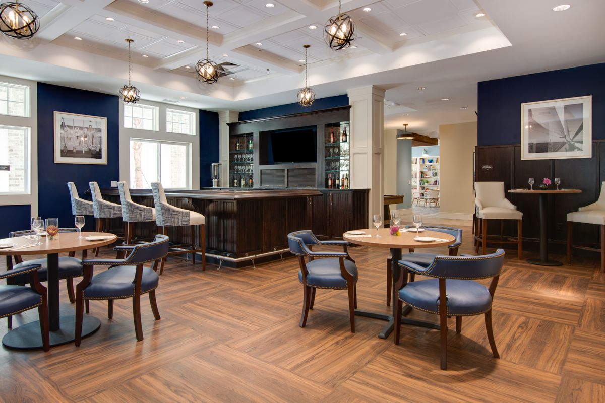 A modern restaurant interior featuring a central bar, tables, and chairs with wood flooring.