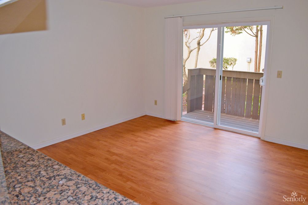 An empty room with hardwood flooring and a sliding glass door leading to a balcony.