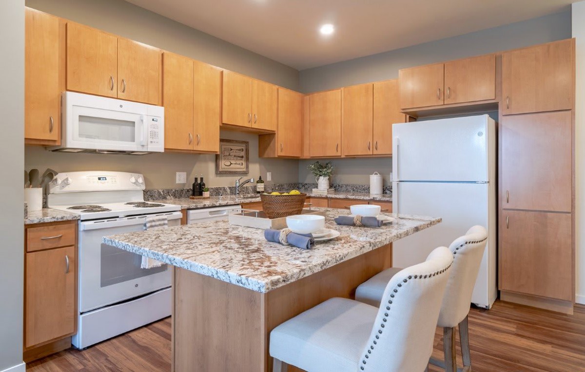 A modern kitchen with granite countertops, wood cabinets, and white appliances.