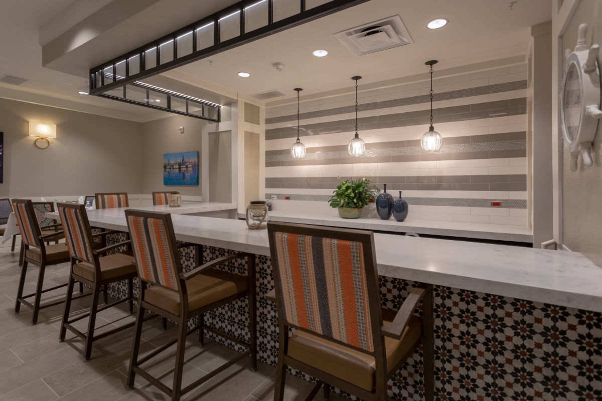 A modern bar interior featuring a sleek counter with high-backed chairs, pendant lighting, and a striped accent wall.