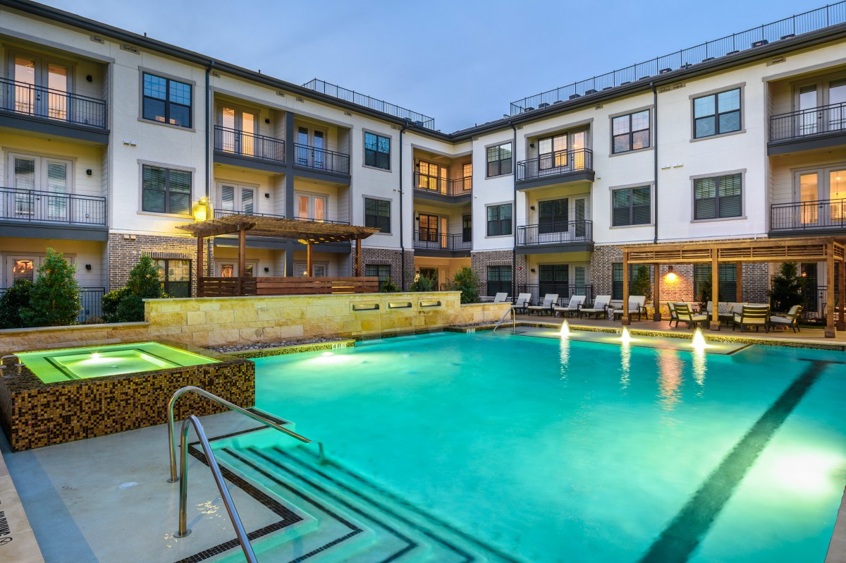 Modern apartment complex with a lit outdoor swimming pool in the evening.