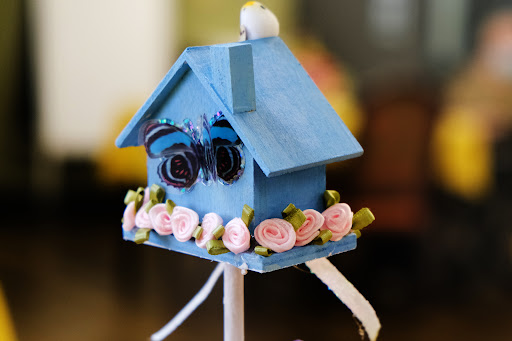 A charming blue decorative birdhouse adorned with delicate pink flowers and a butterfly design.