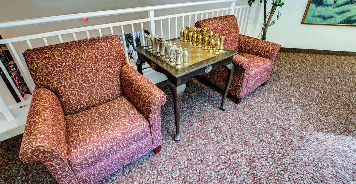 A chessboard set up on a table between two armchairs in an indoor setting.