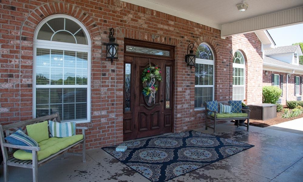 A welcoming front porch with a brick exterior, featuring a decorative wreath on the door, lantern-style lights, and comfortable outdoor seating.